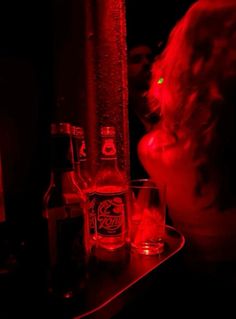 a woman sitting at a table with two glasses and bottles in front of her on the counter