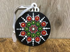 a black round ornament with red, green and white designs on it sitting on a wooden surface