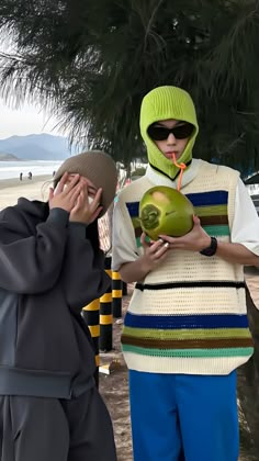 two people standing next to each other near a tree and one is holding a ball