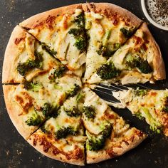 a pizza with broccoli and cheese cut into slices on a black surface next to a fork