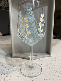 a clear wine glass with yellow and white flowers painted on the side sitting on a counter