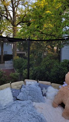 a teddy bear sitting on top of a bed in a yard next to a fence