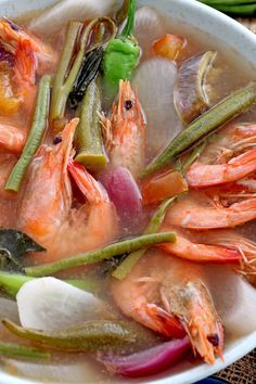 a white bowl filled with soup and shrimp on top of a table next to vegetables