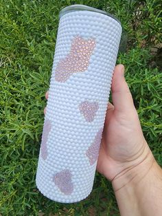 a hand holding a white and pink cup in front of some green grass with hearts on it