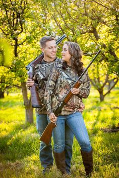 a man and woman holding shotguns in the woods with their backs to each other