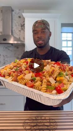 a man holding up a large casserole dish with pasta and vegetables in it