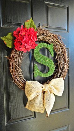 a wreath that has the letter s on it and flowers in front of it, hanging on a door