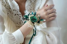 a woman wearing a white shirt and green flower wrist corsage on her arm