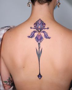 the back of a woman's neck with a purple flower tattoo on her left shoulder