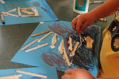 a child is making art with popsicle sticks and glue on the paper that he made