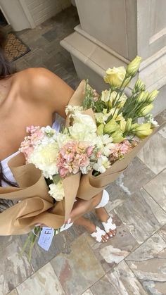 a woman holding a bunch of flowers on top of a tiled floor next to a building