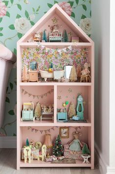 a pink doll house with lots of toys in it's shelves and flowers on the wall