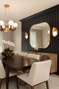 a dining room table with white chairs and a large mirror on the wall above it