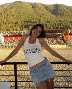 a woman standing on top of a metal rail next to a field with mountains in the background