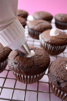 a person is spreading icing on chocolate cupcakes