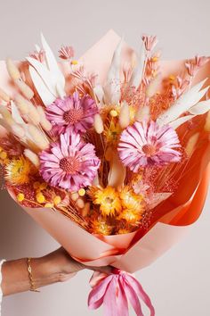 a woman holding a bouquet of flowers in her hand with pink and yellow colors on it