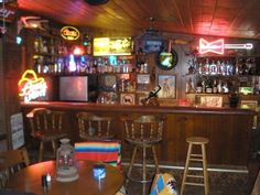 a bar with several stools in front of it and various neon signs on the wall