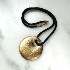 "This is a vintage sterling silver disk pendant necklace.  The disk has a hammered texture and a gold vermeil finish.  It measures 1 7/8\" in diameter.  The pendant hangs from a black twisted chord that is smooth and silky to the touch.  The cord is 18 inches long with a secure sterling vermeil lobster clasp.  The pendant is hallmarked and marked 925 Italy.   This is a vintage, previously owned necklace.  Therefore, light wear can be expected.  There is no visible damage." Elegant Hammered Medallion Necklace, Elegant Hammered Round Medallion Necklace, Hammered Brass Coin Pendant Necklace, Hammered Brass Medallion Coin Necklace, Bronze Hammered Round Pendant Jewelry, Hammered Round Disc Metal Jewelry, Gold Hammered Medallion Necklace, Hammered Brass Coin Necklace, Hand Forged Gold Round Disc Jewelry