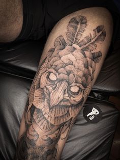 a man's leg with an owl and feathers tattoo design on it, next to a black leather chair