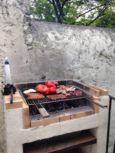 an outdoor grill with meat and vegetables cooking on the outside fire pit, in front of a stone wall