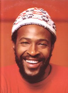 a man with a beard wearing a red shirt and a knitted hat smiles at the camera