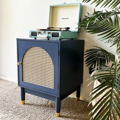 an old fashioned record player sitting on top of a blue cabinet next to a plant