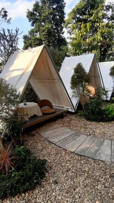 three tents are set up in the middle of a gravel area with trees and bushes