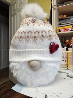 a white knitted hat with a heart on the side and a fur pom - pom attached to it