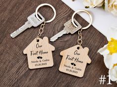 two personalized wooden keychains with house and heart engraved on them, sitting next to a bouquet of flowers