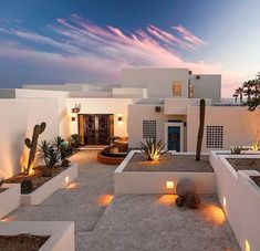 a white house with cactus plants and lights on the front yard at sunset or dawn