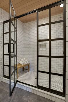 a white tiled bathroom with an open glass door and bench in the shower stall area