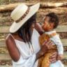 a woman holding a baby in her arms and wearing a hat on top of her head