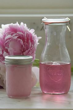 two jars filled with pink liquid next to a bouquet of peonies on a table