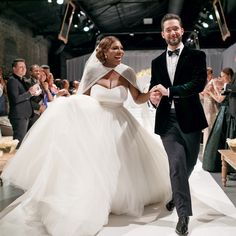 a bride and groom walk down the runway at their wedding ceremony, with guests clapping in the background