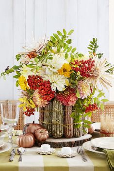 an arrangement of flowers in a wicker basket on a table with plates and utensils