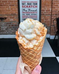 a hand holding an ice cream cone in front of a brick wall and black tile floor