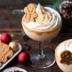 two glasses filled with hot chocolate and topped with whipped cream, gingerbread cookies and sprinkles