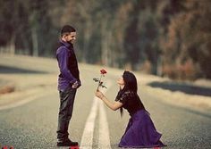 two people standing on the side of an empty road, one holding a flower and the other kneeling down