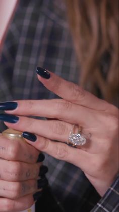 a woman with dark blue nails holding a ring on her finger and looking at the camera