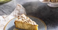 a slice of almond cake on a plate with a fork next to it and another dish in the background