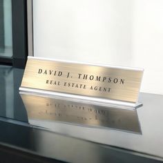 the name plate for david j thompson real estate agent sits on a table in front of a window