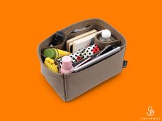 an open gray bag filled with lots of items on top of an orange background,