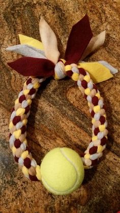 a tennis ball and ribbon bracelet on a rock with a red, white, and yellow bow