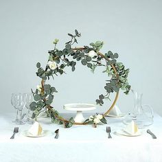 the table is set with white dishes and silverware, including an eucalyptus wreath centerpiece