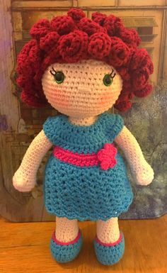 a crocheted doll sitting on top of a wooden table next to a wall