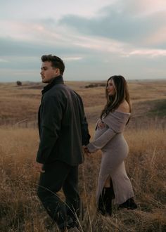 a man and woman holding hands while walking through tall grass in the middle of an open field