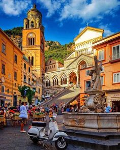 a scooter parked in front of a fountain with people sitting at tables around it