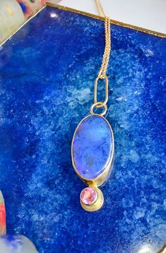 This stunning Lightning Ridge Black Opal is set in an 18k yellow gold bezel on a sterling silver backplate. The opal measures 22 mm by 12 mm. It is accented with a 4 mm Pink Tourmaline set in 18k yellow gold. Chain not included.