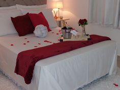 a bed with white sheets and red pillows on top of it next to a lamp