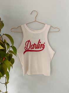 Get all of the southwestern vibes in this Darlin' western inspired retro 90's style cropped tank! - Features the phrase " Darlin' " in a red ink - Screen print transfer that is heat pressed onto each tshirt - Tshirt is a super soft, 90s style micro ribbed baby tee - Regular Baby Tee Fit - Cotton / Poly Blend *due to screens and filters colors may vary slightly to photos* Western Outfit Accessories, Graphic Tee Inspo Design, Americana Graphic Tee, Western Tshirt Designs, 90s Western Fashion, Cool Crop Tops, Farm Merch, Post Punk Fashion, Cute Clothes Aesthetic